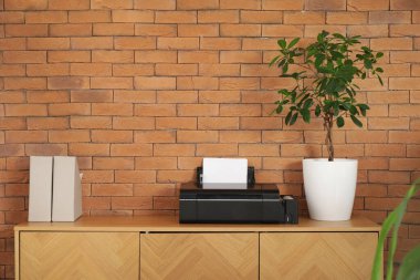 Ofisteki tuğla duvarın yanında modern yazıcı ve fabrika var.