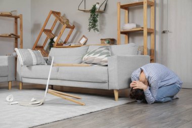 Deprem sırasında oturma odasında kanepede saklanan korkmuş genç bir kadın.