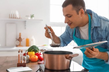 Genç adam mutfakta çorba tadıyor.