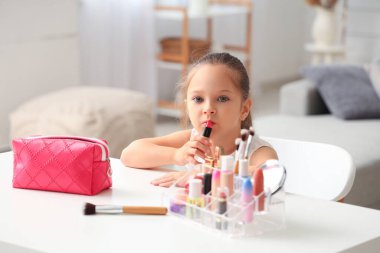 Oturma odasındaki makyaj malzemeleri ve kozmetik çantasıyla sevimli küçük bir kız.