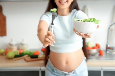 Mutfakta taze sebze salatası ve çatallı genç hamile kadın.