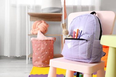 Çocuk odasında sandalyesinde oyuncak tavşanlı leylak sırt çantası, yakın plan.