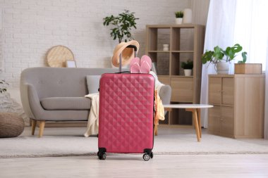 Oturma odasında şapka ve parmak arası terliklerle dolu bavul.