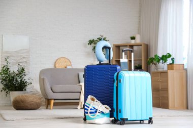 Oturma odasının içinde boyun yastığı ve plaj çantası olan bavullar.