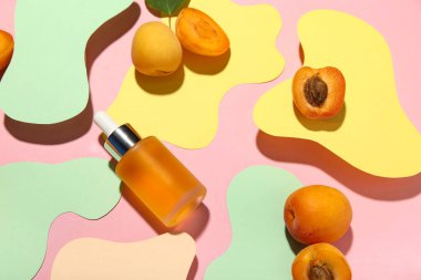 Renkli arka planda taze kayısıları olan bir şişe kozmetik yağı.