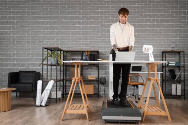 Ofisteki koşu bandında dizüstü bilgisayarla çalışan yakışıklı bir iş adamı.