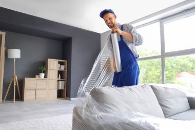 Erkek işçi kanepeyi streç filmle kaplıyor.