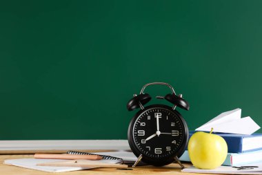 Elma, çalar saat, kitaplar ve karatahtanın yanındaki masada kağıt uçak. Okul konseptine dönelim.