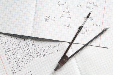 El yazısıyla yazılmış matematik formülleri ve arka plan olarak bir çift pusula, yakın plan kitaplarıName