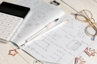 El yazısı matematik formülleri, hesap makinesi ve beyaz ahşap zemin üzerine kırtasiye defteri