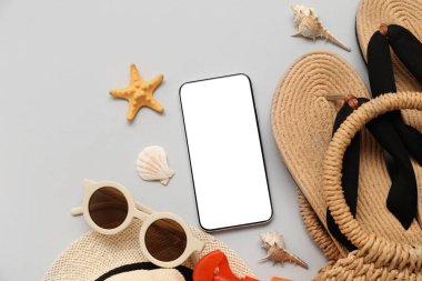 Cep telefonu ve gri arka planda parmak arası terlikleri olan plaj aksesuarları. Üst görünüm