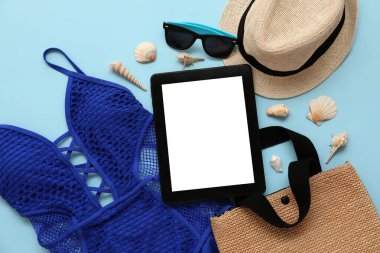 Mavi arka planda mayolu plaj aksesuarları ve tablet. Üst görünüm