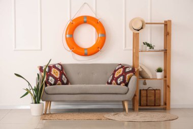 Yastıklı rahat kanepe, raf ünitesi, ev bitkisi ve oturma odasında can simidi halkası.