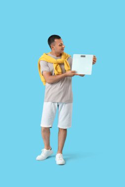 Mavi arka planda ağırlık tartısı olan genç bir adam.