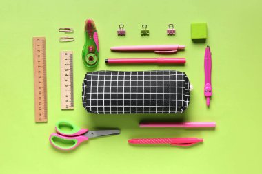 Yeşil arka planda farklı kırtasiye malzemesi olan siyah kareli kalem kutusu. Üst görünüm