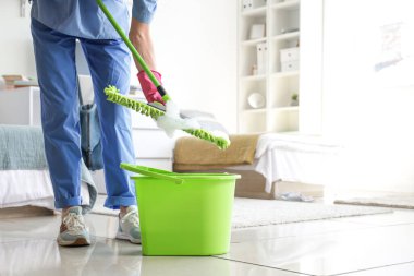 Yurt odasında paspas ve kova taşıyan hademe.