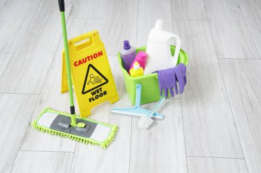 Çamaşır odasındaki ıslak zemini gösteren uyarı işareti ile temizlik malzemeleri.