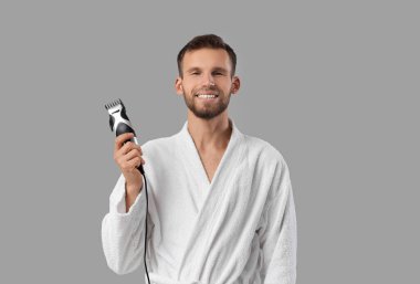 Gri arka planda elektrikli budayıcısı olan sakallı genç adam.