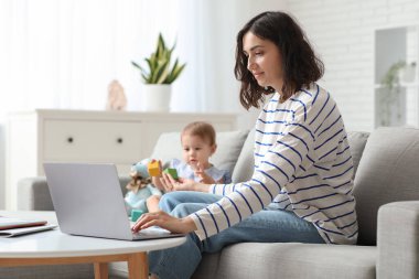 Sevimli bebek ve evde doğum izninde dizüstü bilgisayarla çalışan mutlu genç anne.