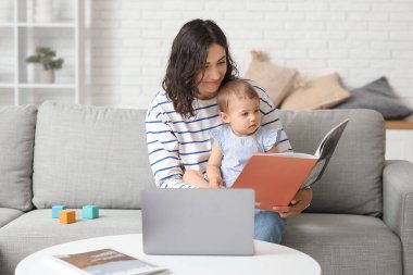 Evde doğum izninde olan sevimli bebek tutma dergisi ve dizüstü bilgisayarıyla mutlu genç bir anne.