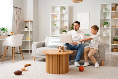 Mutlu küçük oğlu ve babası evdeki kanepede dizüstü bilgisayarla çalışıyorlar.