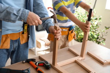 Babası ve küçük oğlu farklı enstrümanlarla evde mobilya monte ediyorlar.