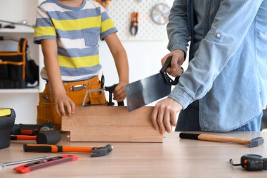 Baba ve küçük oğlu farklı aletlerle evde ahşap mobilya monte ediyorlar.