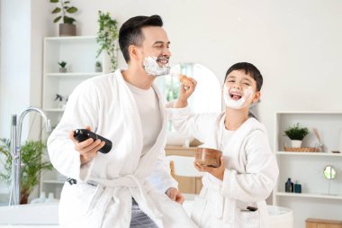 Mutlu baba ve küçük oğlu banyoda tıraş köpüğüyle fırça tutuyorlar.