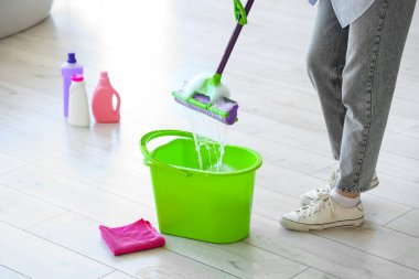 Kovalı ve deterjanlı genç bir kadın evde yerleri paspaslıyor.