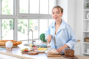 Güzel, genç ve mutlu bir kadın evde tereyağlı tost ekmeği kesiyor.