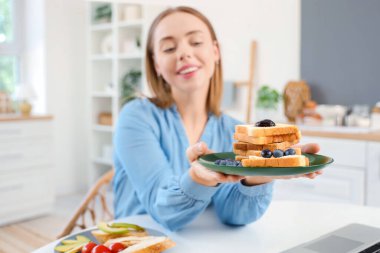 Güzel, genç ve mutlu bir kadın evde taze tereyağı, avokado ve yabanmersini ile lezzetli tostlar tutuyor.