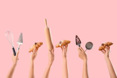 Farklı pişirme aletleri ve pembe arka planda lezzetli kruvasanları olan kadın elleri.