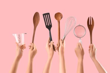 Pembe arka planda farklı pişirme aletleri olan kadın elleri.