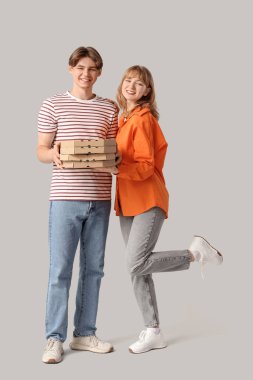 Gri arka planda lezzetli pizzalarla dolu karton kutular taşıyan güzel genç bir çift.