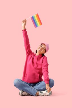 Pembe arka planda oturan LGBT bayrağıyla güzel genç bir kadın.