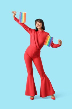 Beautiful young woman with LGBT flags on blue background