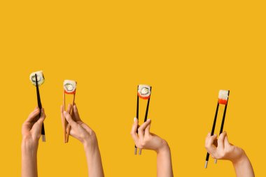 Kadın elleri yemek çubuklarını tutarken sarı arka planda farklı lezzetli suşi ruloları yapıyor.