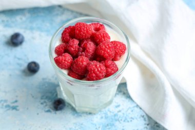 Taze ahududu ve açık mavi arkaplanda yabanmersini ile bir bardak lezzetli yoğurt.
