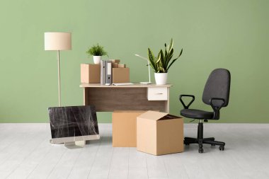 Taşınma gününde iş yerindeki yeşil duvarın yanında karton kutular ve sandalye.