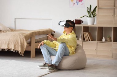 Genç çocuk yatak odasında VR gözlüğü kullanıyor.