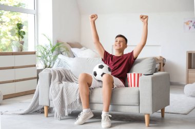 Evdeki kanepede futbol maçı izleyen mutlu ergen çocuk.