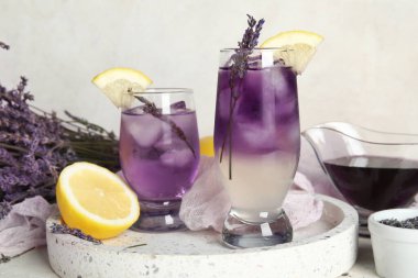 Açık arkaplanda soğuk lavantalı limonata, çiçek ve şurup bardakları.