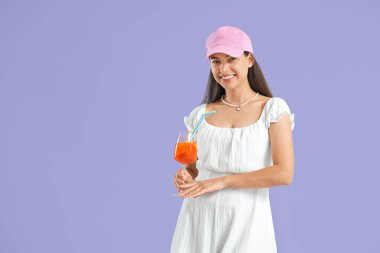 Leylak arka planında aperol sprey kokteyli olan şapkalı genç bir kadın.