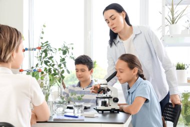 Genç kız okulda biyoloji dersinde öğretmenle mikroskoptan bakıyor.