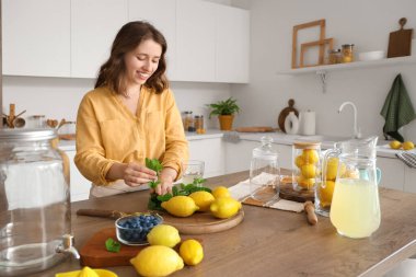 Genç kadın mutfaktaki limonataya nane şekeri ekliyor.