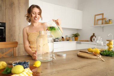 Genç bir kadın mutfakta kavanoza limonata dolduruyor.