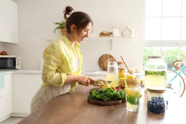 Mutfaktaki masada limonata için limon kesen genç bir kadın.