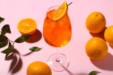 Portakallı ve pembe arka planda yapraklı bir bardak Aperol sprey kokteyli.