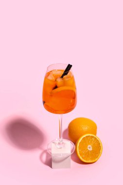 Pembe arka planda bir bardak Aperol spreyli kokteyl ve portakallar.