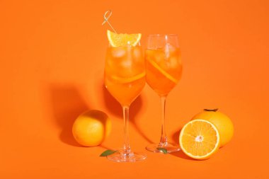 Bir bardak Aperol spreyli kokteyl ve turuncu arka planda meyveler.